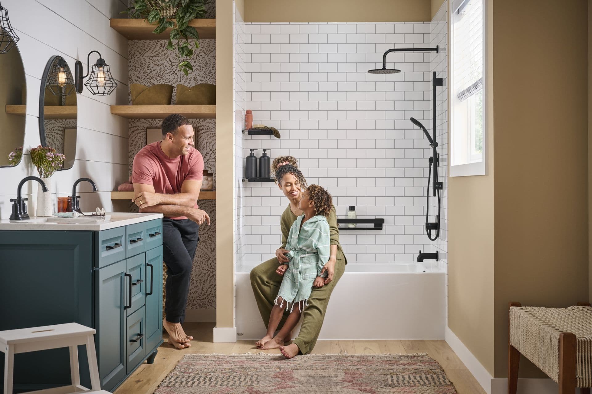 Man, woman, and child in modern bathroom with white subway tile shower, black fixtures, and teal vanity with open shelving.